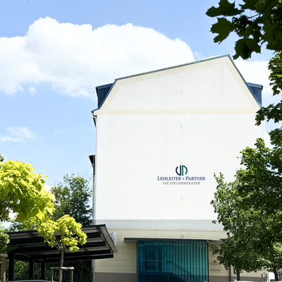 Ansicht des Kanzleigebäudes von Lehleiter + Partner auf der Emmerichstraße 51 mit Logo auf dem Giebel und großem Parkplatz.