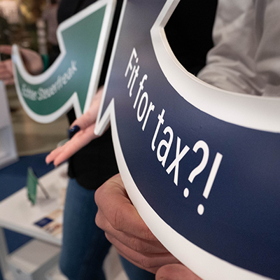 Zwei Steuerfachangestellte stehen am Messestand von Lehleiter + Partner und halten Schilder als Pfeile in der Hand. Auf dem blauen steht: Fit for tax?!