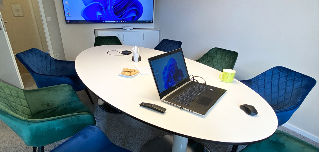Besprechungszimmer von Lehleiter + Partner in Görlitz mit grünen und blauen gemütlichen Sesseln um den Tisch, einem Laptop und großem Bildschirm an der Wand.