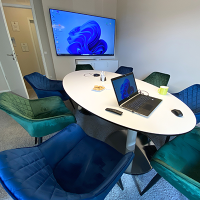 Besprechungszimmer von Lehleiter + Partner in Görlitz mit grünen und blauen gemütlichen Sesseln um den Tisch, einem Laptop und großem Bildschirm an der Wand.